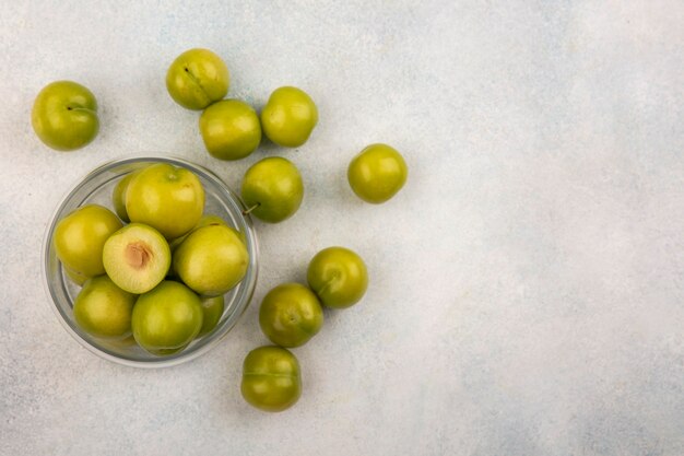 Top view of green plums in jar and on white background with copy space