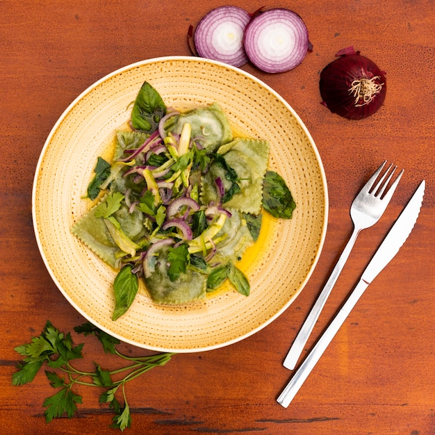 Top view of green ravioli with onion and basil leaves wooden table