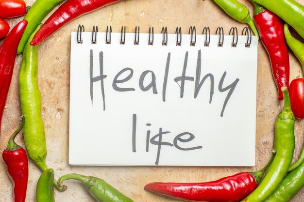 Top view green and red peppers healthy life written on notepad on amber background