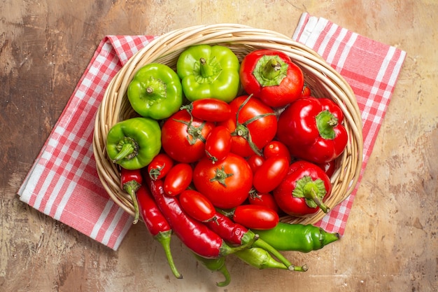 Top view green and red peppers hot peppers tomatoes in wicker basket and kitchen towel on amber background
