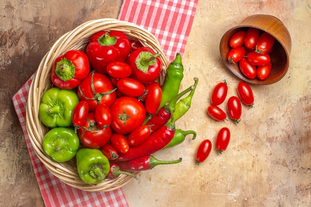 Top view green and red peppers hot peppers tomatoes in wicker basket scattered cherry tomatoes from bowl kitchen towel on amber background