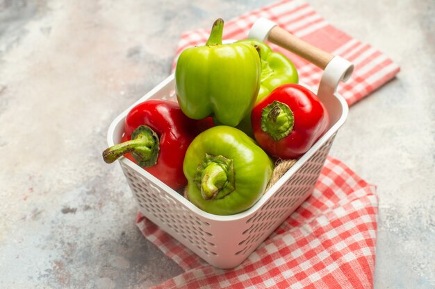 Top view green and red peppers in plastic basket red white checkered tablecloth on nude surface
