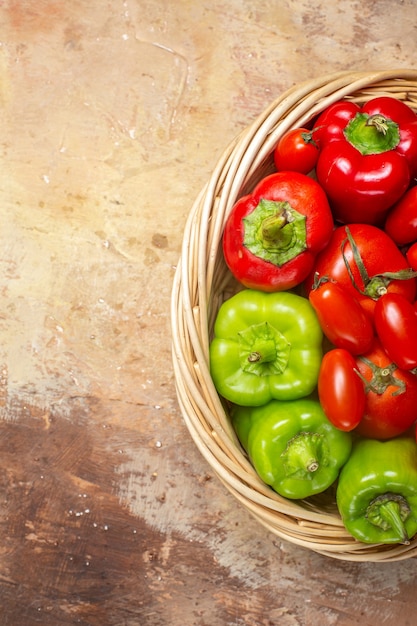 Top view green and red peppers and tomatoes in wicker basket on amber background