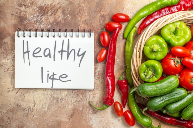 Top view green and red peppers tomatoes in wicker basket cherry tomatoes healthy life written on notepad on amber background