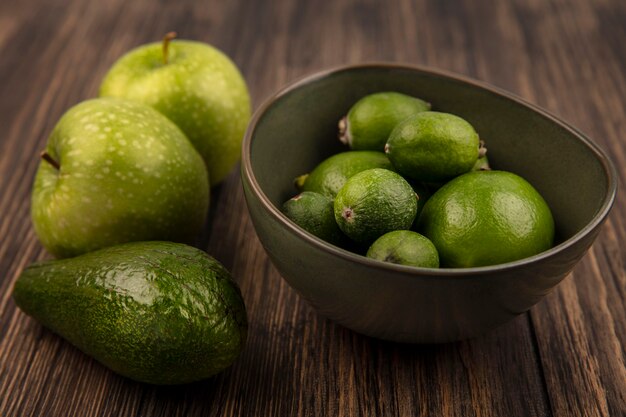 Top view of green ripe feijoas with limes on a bowl with green apples and avocado isolated on a wooden wall