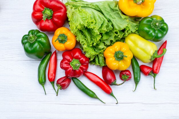 top view of green salad along withful bell peppers and spicy peppers on white desk,  vegetable food meal ingredient