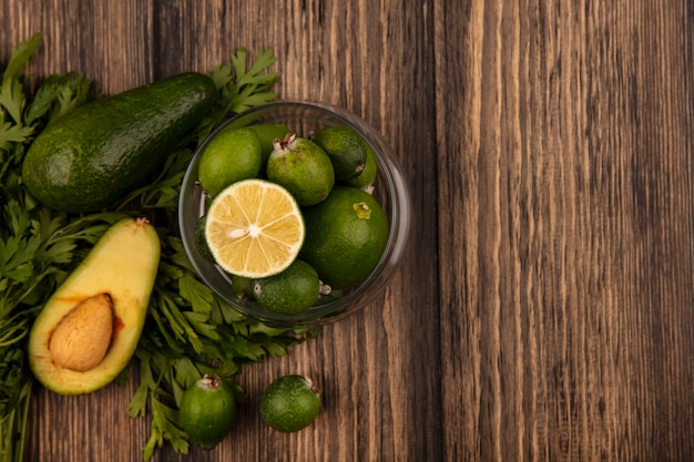 Top view of green skinned feijoas with limes on a glass bowl with avocado feijoas and parsley isolated on a wooden surface with copy space