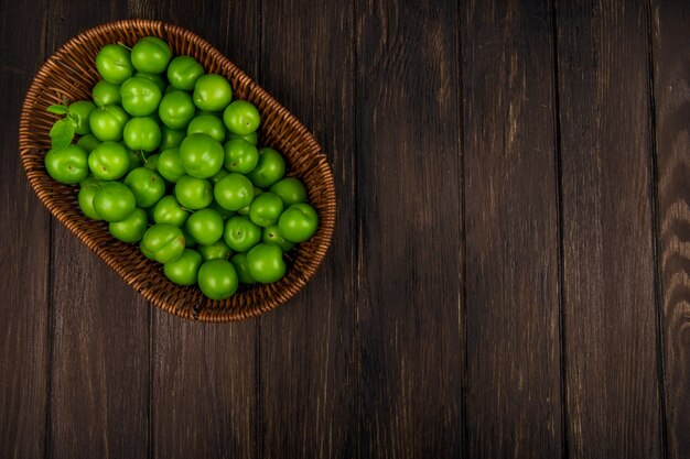 Top view of green sour plums in a wicker basket on dark wooden table with copy space