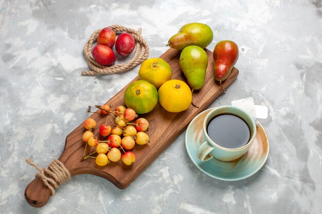 Top view green tangerines with sweet cherries plums tea and pears on light white desk.