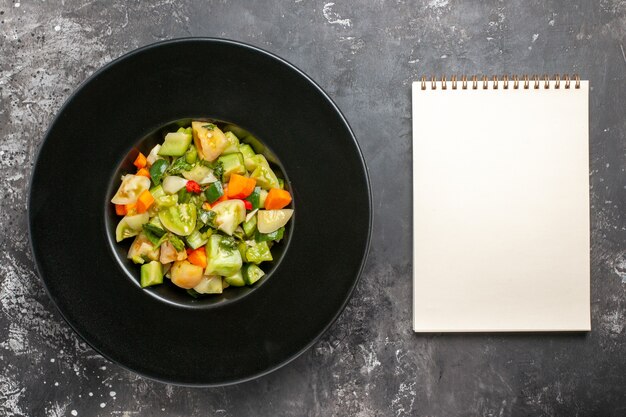 Top view green tomato salad on black oval plate notepad on dark background