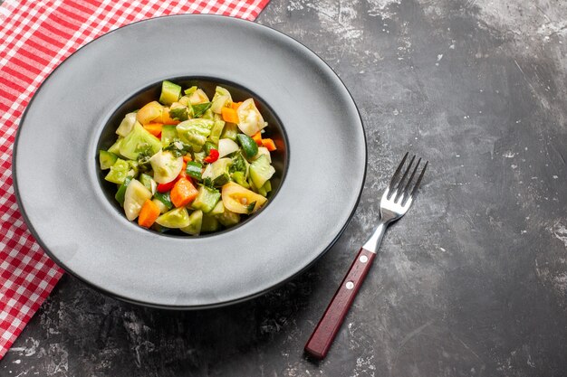 Top view green tomato salad on grey oval plate a fork on dark background