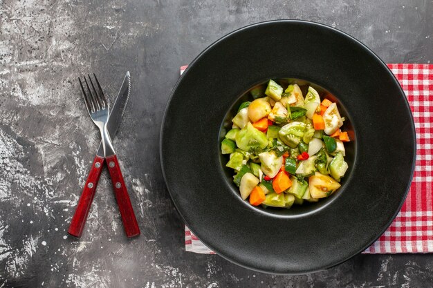 Top view green tomato salad on oval plate crossed knife and a fork on dark background