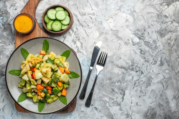 Top view green tomato salad on oval plate on cutting board a fork a knife on dark background