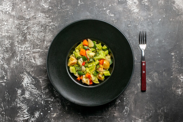 Top view green tomato salad on oval plate a fork on dark background