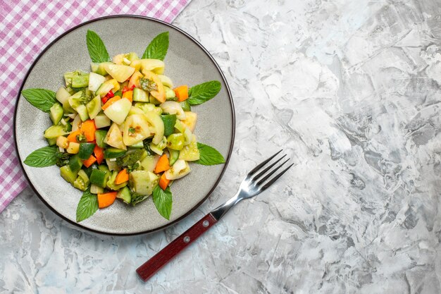 Top view green tomato salad on oval plate a fork on dark background