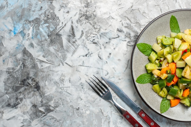 Top view green tomato salad on oval plate fork and knife on grey background