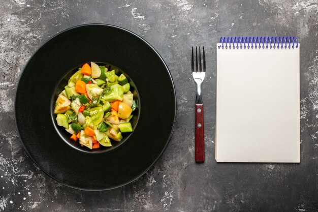 Top view green tomato salad on oval plate a fork notebook on dark background