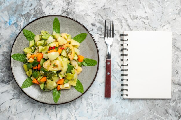 Top view green tomato salad on oval plate a fork notepad on grey background