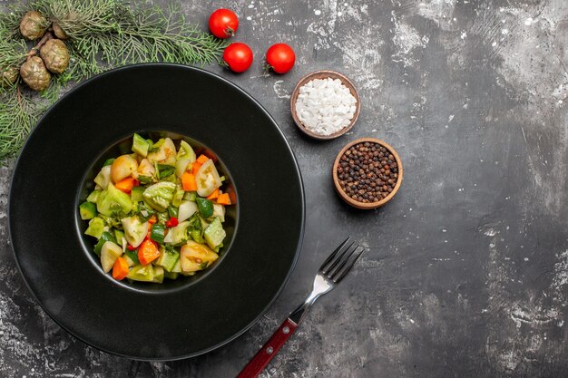 Top view green tomato salad on oval plate a fork salt and black pepper on dark background