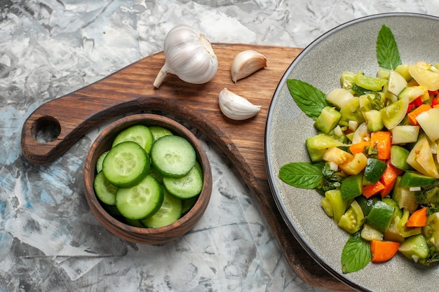 Foto gratuita insalata di pomodori verdi vista dall'alto su piatto ovale aglio su tagliere ciotola con cetrioli tagliati su sfondo scuro