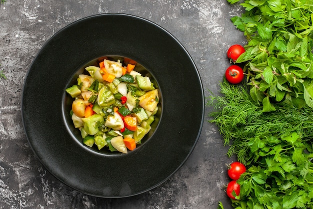 Top view green tomato salad on oval plate greens tomatoes on dark background