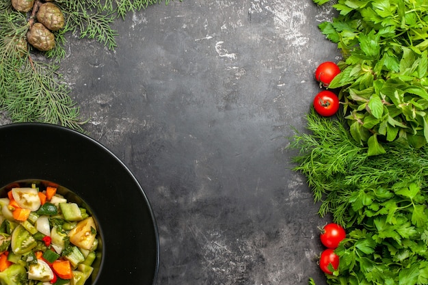 Вид сверху салат из зеленых помидоров на овальной тарелке зелень помидоры на темном фоне