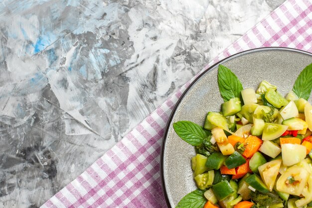 Top view green tomato salad on oval plate pink tablecloth on grey background free space