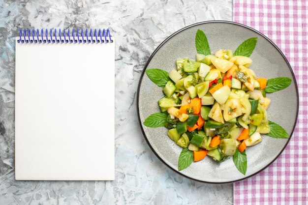 Top view green tomato salad on oval plate pink tablecloth a notebook on grey surface