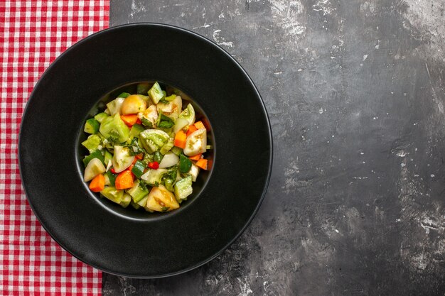 Top view green tomato salad on oval plate red white checkered tablecloth on dark surface