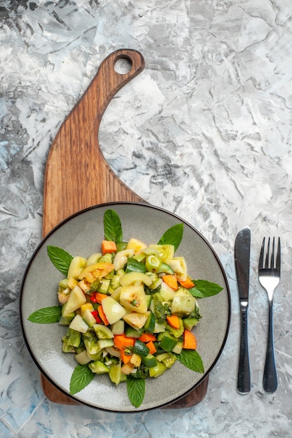 Free photo top view green tomato salad on oval plate on serving board a fork knife on dark background