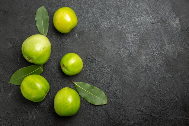 Top view green tomatoes and bay leaves on the left of dark surface