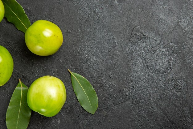 Top view green tomatoes bay leaves on the left of dark surface