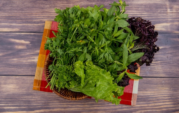 Top view of green vegetables in basket on cloth on wooden surface