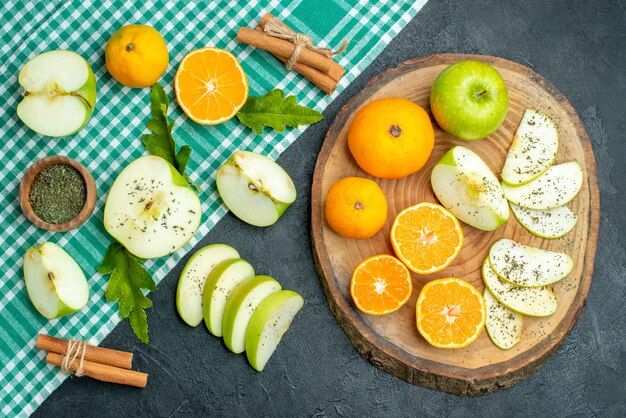 Top view green white tablecloth cut fruits apples oranges on wood board cinnamons on dark background