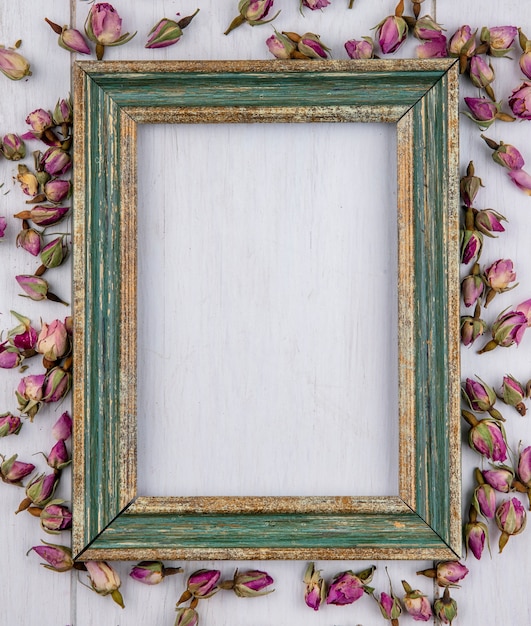 Free photo top view of greenish gold frame with dried purple rosebuds on a white surface