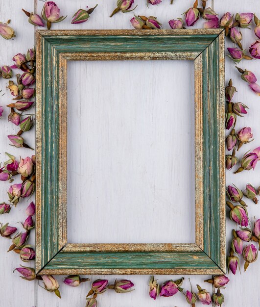 Top view of greenish gold frame with dried purple rosebuds on a white surface