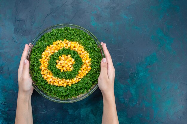 Top view greens salad with corns inside round glass plate on the dark-blue desk.