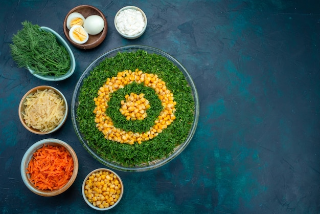 Top view greens salad with corns inside round glass plate with eggs and sliced carrots on dark-blue desk.