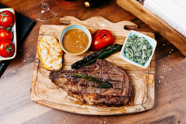 Top view of griled beef steak served with vegetables and sauce on a wooden board