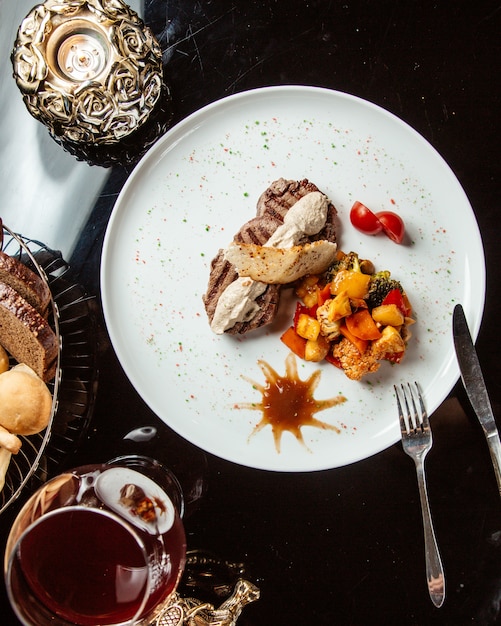 Top view of grilled beef medallion with sauce and vegetables on a white plate on the table