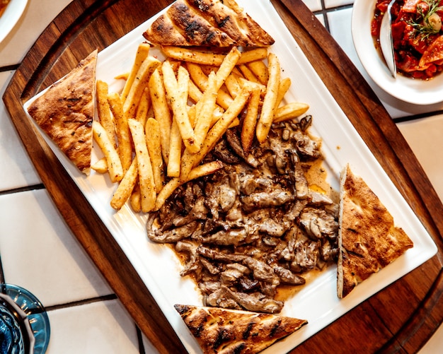 Top view of grilled beef pieces served with french fries and toasted tandoor bread