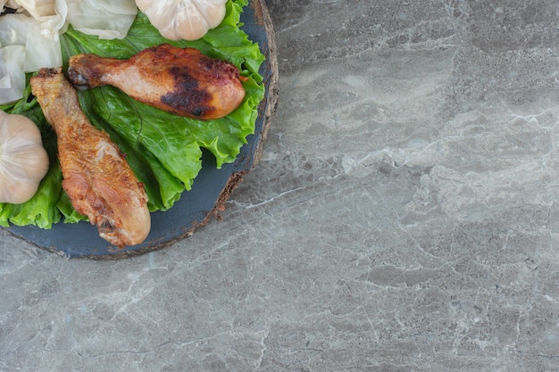 Top view of grilled chicken drumstick on lettuce leaves.