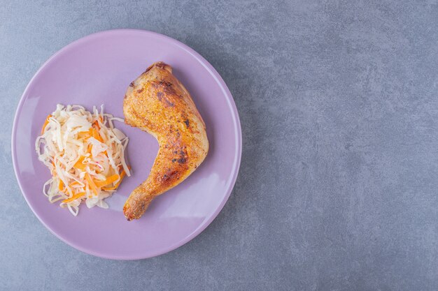 Top view of grilled chicken leg with pile of sauerkraut on purple plate.