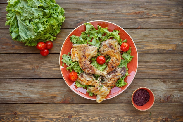 Top view of grilled chicken legs served on lettuce leaves with cherry tomates