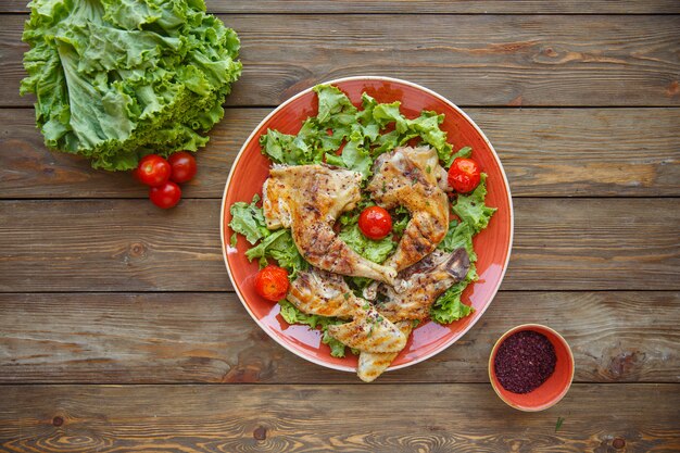 Top view of grilled chicken legs served on lettuce leaves with cherry tomates