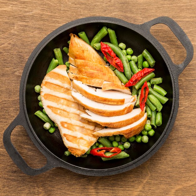 Top view grilled chicken and peas in pan with chilli peppers