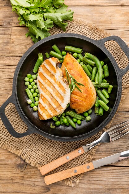 Top view grilled chicken and peas in pan with cutlery