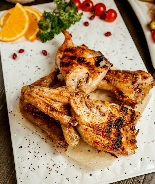 Top view of grilled chicken served with orange slice tomato and herbs