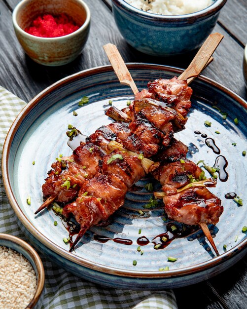 Top view of grilled chicken skewers with soy sauce on a plate on wood