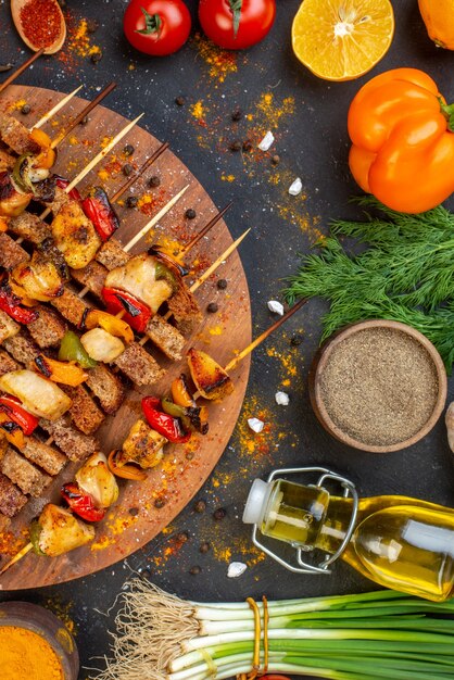 Top view grilled chicken skewers on wooden board and other stuffs on dark table